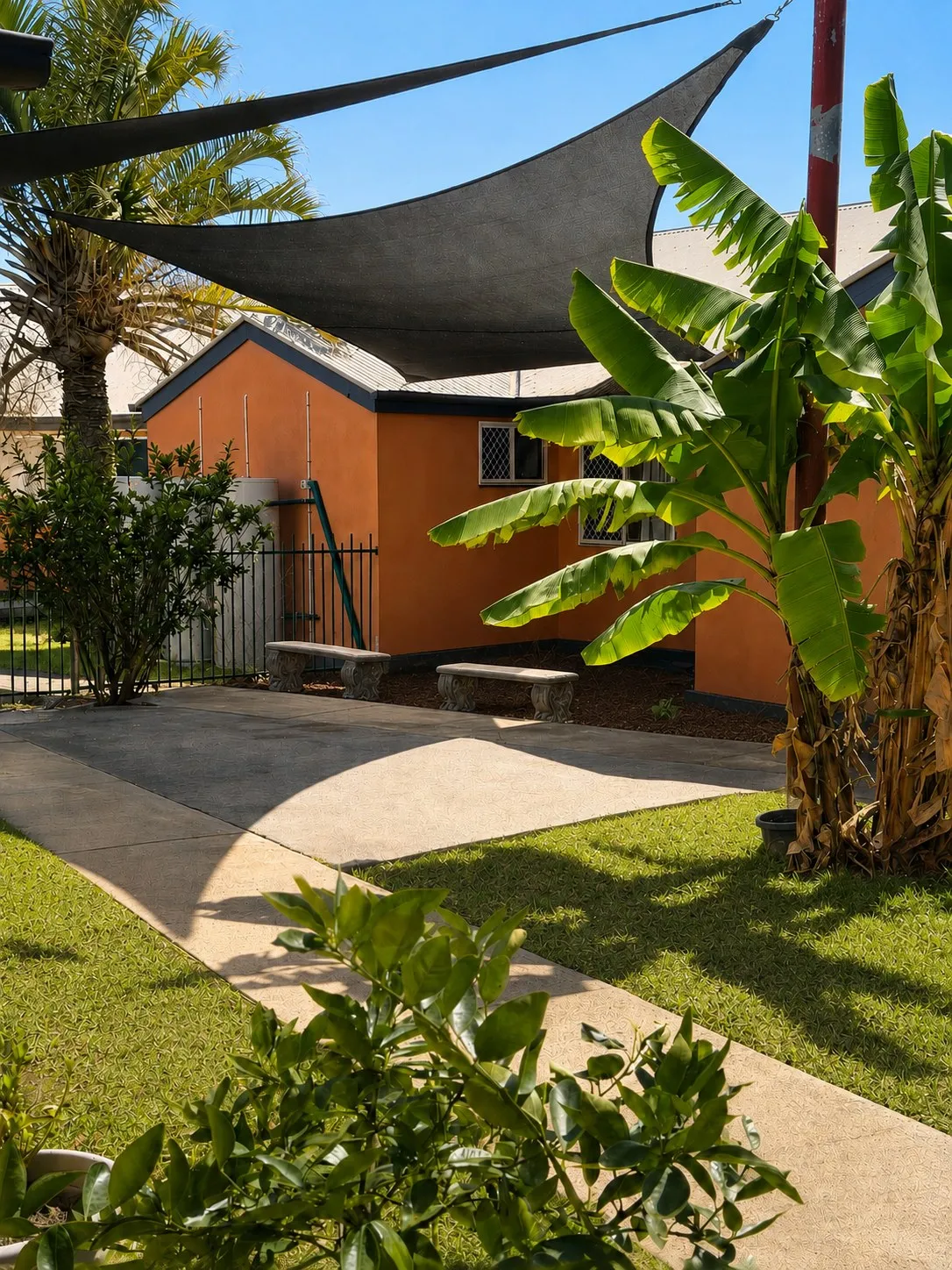 Shade sail over the courtyard garden with bench seating and banana palms at Christine Court